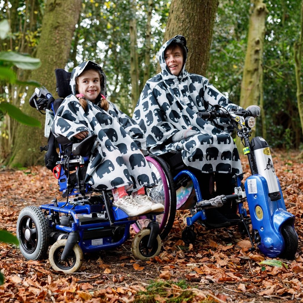 Kids Wheelchair poncho - easy to put on, fully waterproof and with peaked hood to protect faces from the rain. Seen here in an elephant design with the adult wheelchair poncho in the same design.