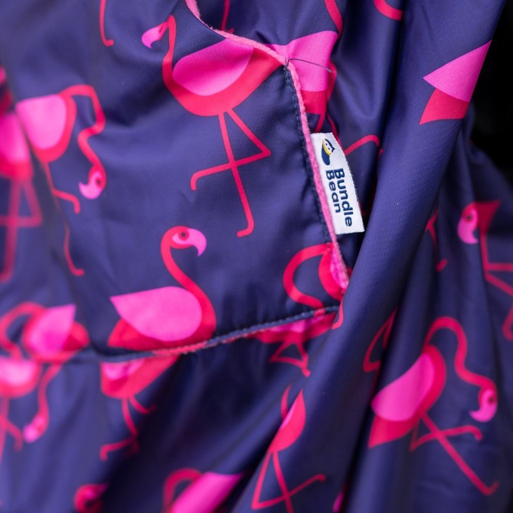 Kids fleece-lined wheelchair cosies. Waterproof, warm and easy to fit. Seen here in a flamingo design and showing the hand warming pocket.
