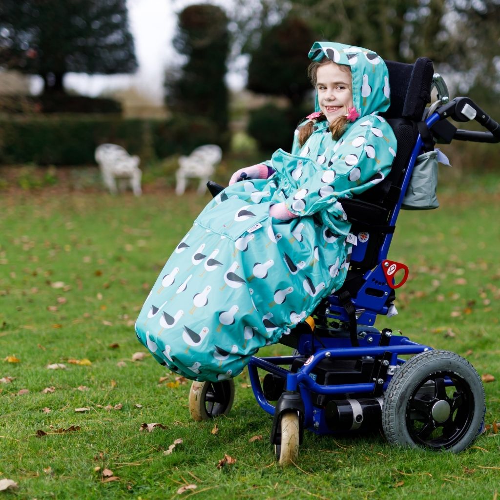 Kids fleece-lined wheelchair cosies. Waterproof, warm and easy to fit. Seen here in a silver lightning design with protective rainhood up.